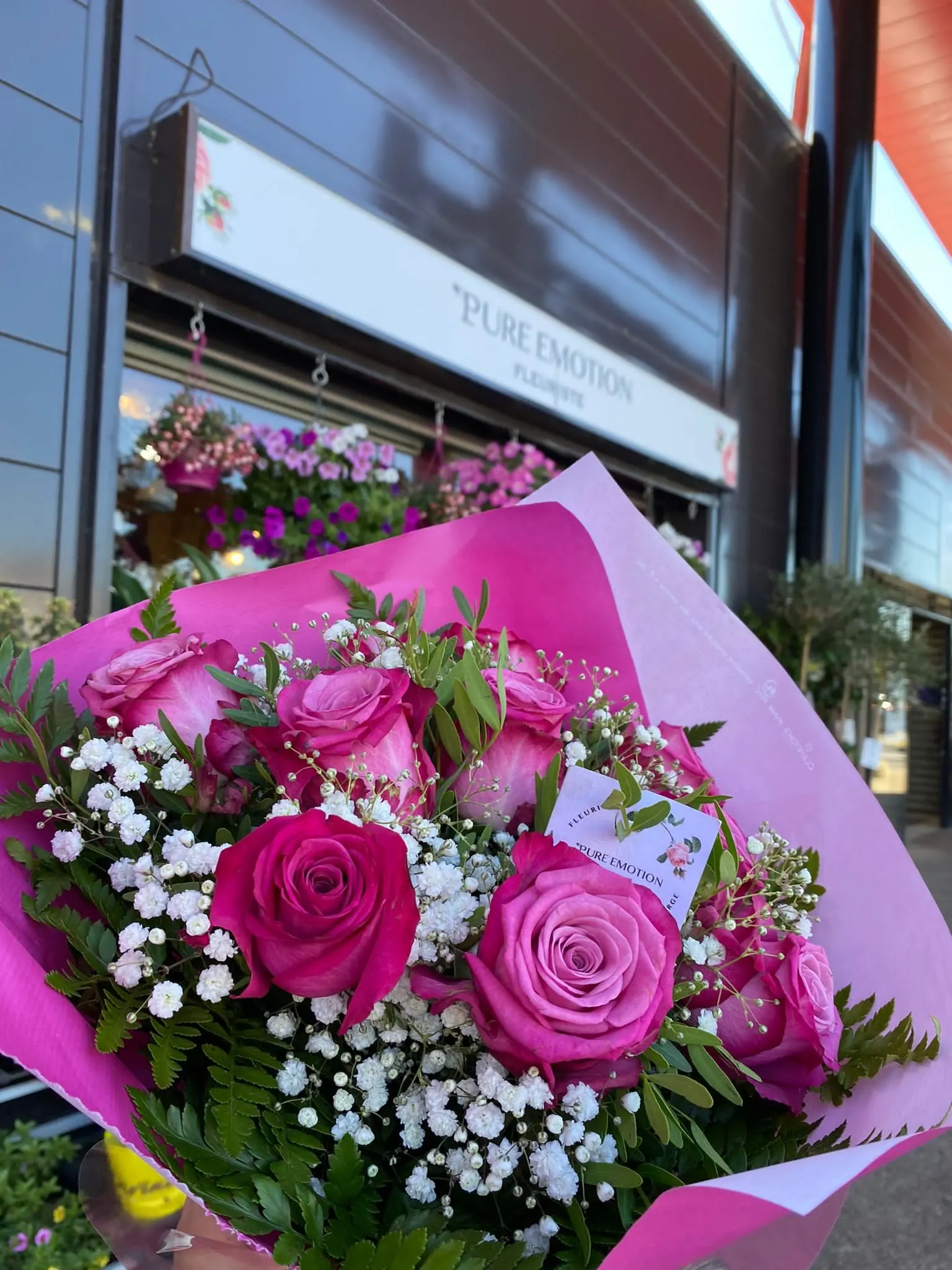 Bouquet de roses fuchsia et de gypsophile dans un papier rose, devant la boutique Pure Émotion